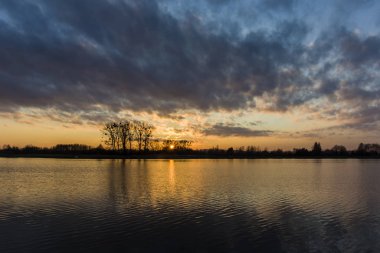 Suyun üzerinde akşam bulutları ve renkli gökyüzü ile gün batımı