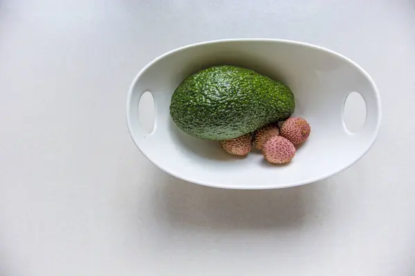 Зеленый авокадо и личи в белой чашке на белом фоне — стоковое фото