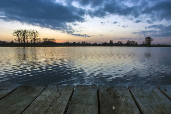 Nuvens sobre o lago após o pôr do sol e uma ponte de madeira — Fotografia de Stock