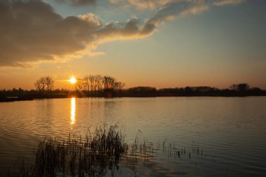 Sakin bir göl üzerinde güneş ve bulut batıyor, akşam manzarası