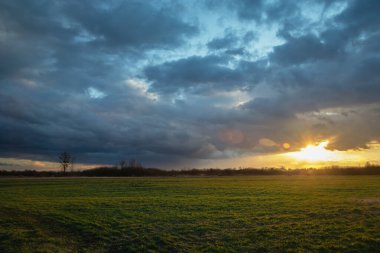 Yağmurlu gökyüzü ve gün batımı yeşil çayırın üzerinde