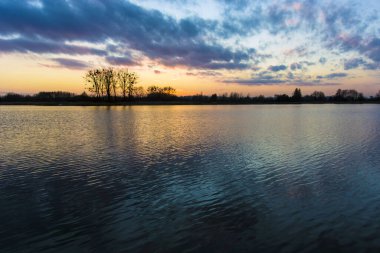 Gölün üzerinde gün batımından sonra renkli bulutlar, ufukta ağaçlar, Stankow, Lubelskie, Polonya