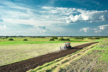 Çekici tarlayı sürüyor, ufukta ve mavi gökyüzünde beyaz bulutlar