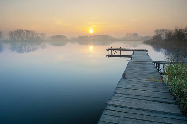 Langer Holzsteg Auf Einem Ruhigen Und Nebligen See Bei Sonnenuntergang — Stockfoto