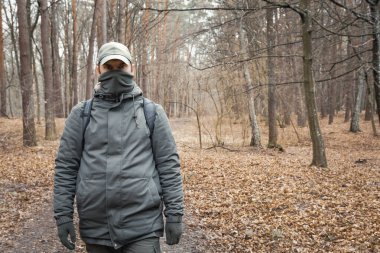 Yüzü kapalı bir adam sonbahar ormanında yürüyor.