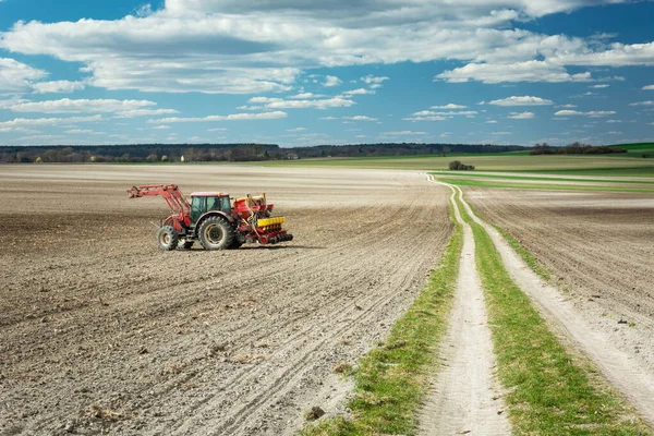 Tarlalı bir tarlada tarım traktörü, uzun toprak bir yol ve mavi gökyüzünde beyaz bulutlar..