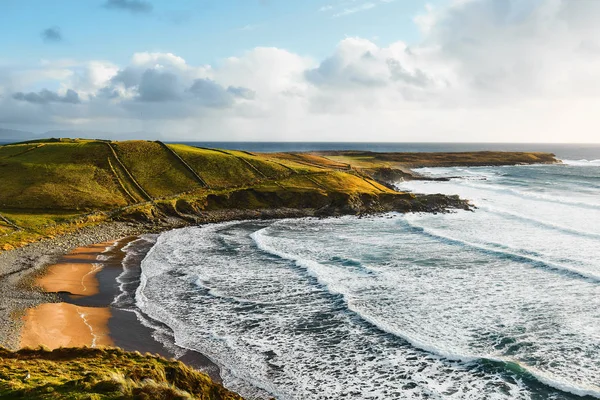 Irish beach during sunset in the summer with a blue sky and waves smashing against the rocks Royalty Free Stock Images