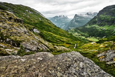 Yol üzerine yeşil mera zirveleri ve karanlık bulutlu gökyüzü kar ile Batı Norveç dağlarında 