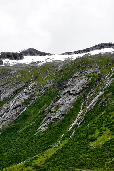 Berge und Wasserfälle in Norwegen mit Schnee und grünem Gras bedeckt — Stockfoto