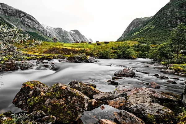 Bergdorf mit kleinen Häusern und Holzhütten mit Gras auf dem Dach in einem Tal. Die Hütten stehen auf grünem Gras und Weide. Die Berge sind mit Schnee bedeckt. Langzeitbelichtungsbild. — Stockfoto