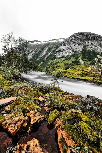 Longa exposição de casas de telhado de grama nas montanhas da Noruega com prados verdes e um rio de água branca em primeiro plano — Fotografia de Stock
