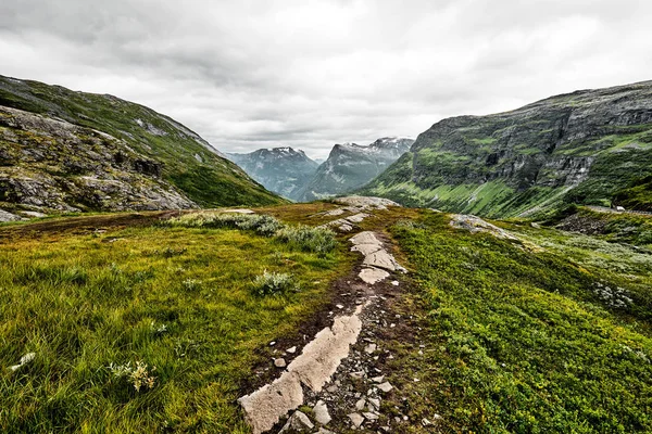 Yol üzerine yeşil mera zirveleri ve karanlık bulutlu gökyüzü kar ile Batı Norveç dağlarında