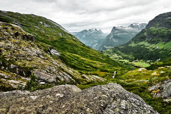 Caminho sobre pasto verde nas montanhas da Noruega Ocidental com neve nos cumes e um céu escuro e nublado — Fotografia de Stock