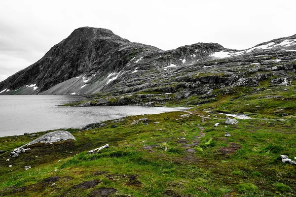 Grama verde e água nas montanhas do norway com cumes cobertos de neve e um lago — Fotografia de Stock