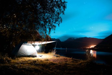 Dağlar, bir şehir ve uzakta Norveç'te mavi gökyüzü ile gece fiyort kamp 