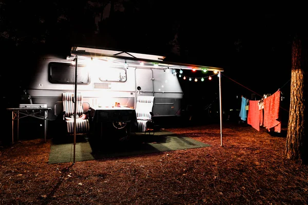 Retro vintage kamp karavan römork gece ışıklar, sandalye ve bir tablo ile bir ormanda