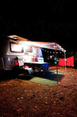 Retro vintage kamp karavan römork gece ışıklar, sandalye ve bir tablo ile bir ormanda