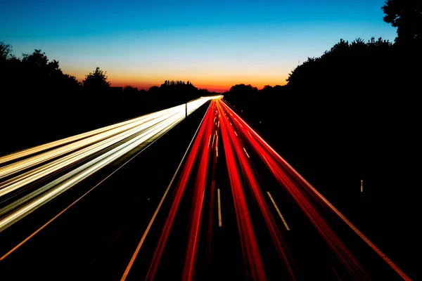 Uzun pozlama görüntü kırmızı ve beyaz ışık yollar ve arka planda renkli bir gün batımı ile Almanya Gelsenkirchen A2 otoyolunun