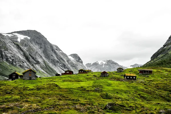 美丽的自然斑点与河 石头和牧场在被积雪覆盖的山围拢的谷 五颜六色的房子矗立在绿色的草地上 位于挪威的 Geiranger 和卑尔根之间 — 图库照片