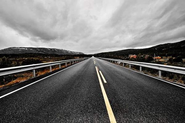 geniş açık bir çayır ve dağlar göz kış döneminde karanlık bulutlu gökyüzü altında güzel doğa ile görebilirsiniz kadarıyla uzanan bir asfalt Otoban yol ile görüntü     