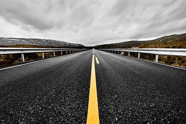 geniş açık bir çayır ve dağlar göz kış döneminde karanlık bulutlu gökyüzü altında güzel doğa ile görebilirsiniz kadarıyla uzanan bir asfalt Otoban yol ile görüntü     
