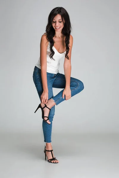 Getting dressed for tonight. Full length of beautiful young woman adjusting her shoe with smile while standing against white background