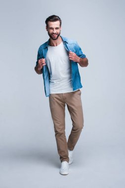 Gitmeye hazırım! Tam uzunlukta yakışıklı genç adam kameraya bakıyor ve hisshirt gülümseme duran beyaz arka plan ile ayarlama