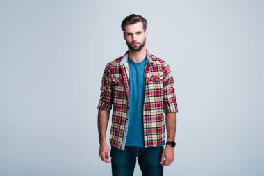 Bütün ayrıntılara dikkat. Yakışıklı genç adam ayakta beyaz arka planı süre kamera bakarak Kareli gömlekli