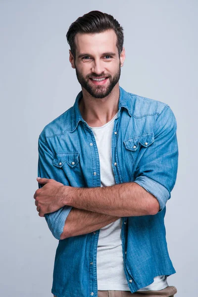 Sırdaş gülümseme. Gülümseyerek kameraya bakıyor ve beyaz arka plan karşı duran armscrossed tutmak yakışıklı delikanlı