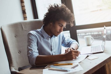 Konsantre ve yakışıklı. Yakışıklı genç işadamı ofis masasında otururken bir şey yazma yan görünüm