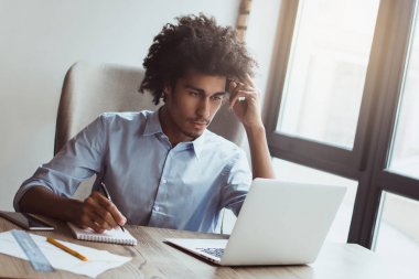 İş yerinde planlama. Bir şey yazma ve ofis masasında otururken diz üstü kullanma yakışıklı genç işadamı