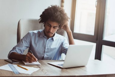 İş yerinde uzmanlık. Yakışıklı genç işadamı ofis masasında otururken bir şey yazma