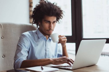 Kahve iş sırasında. Onun laptop kullanma ve içme kahve ofis masasında otururken yakışıklı genç işadamı