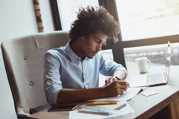 Konsantre ve yakışıklı. Yakışıklı genç işadamı ofis masasında otururken bir şey yazma yan görünüm