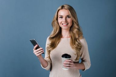 Kahve molası zamanı. Telefonunu kullanarak ve gülümseme duran siyah arka plan ile kameraya bakarak güzel genç kadın