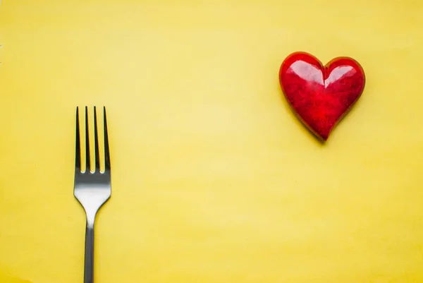 Love for dessert. Top view of a fork and read heart against yellow background