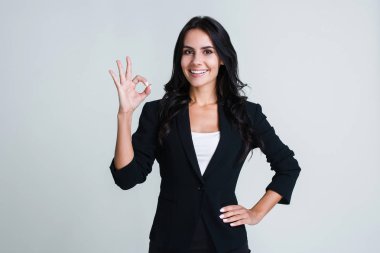 Her şey mükemmeldir. Kameraya bakarak ve Tamam gülümseme duran beyaz arka plan ile el hareketi güzel genç iş kadını