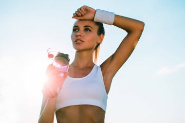 Küçük dinlenme. Genç güzel kadın uzağa bakıyor ve onun sporcu içmek şehir manzaralı karşı dururken tutan spor giyim