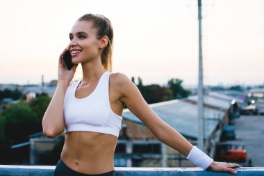 Duyduğuma sevindim! Spor giyim sanayi kenti görünümü gündoğumu ile karşı dururken gülümsemeyle onun smartphone kullanarak genç güzel kadın