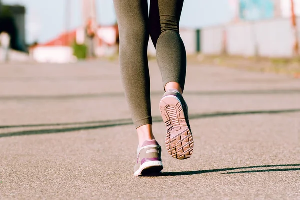 Running to success. Close-up rear view of young fit woman in sportswear jogging against industrial city view