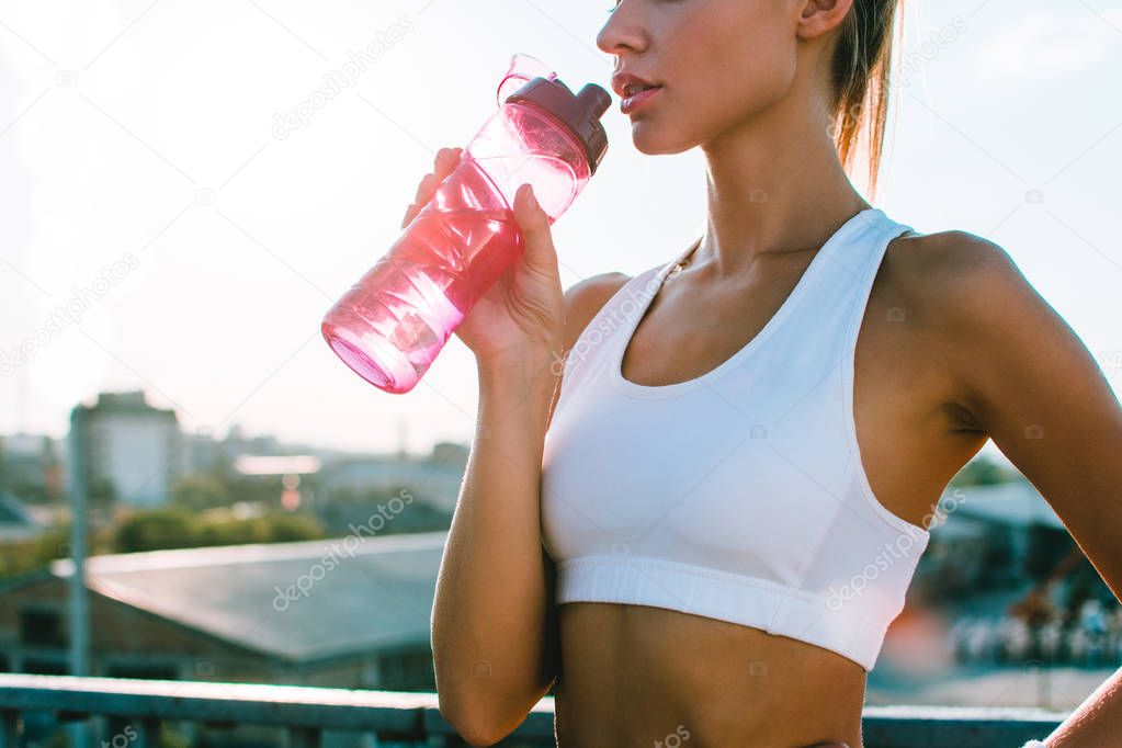 Sip of freshness. Part of young beautiful woman in sportswear drinking her sports drink while standing against city view