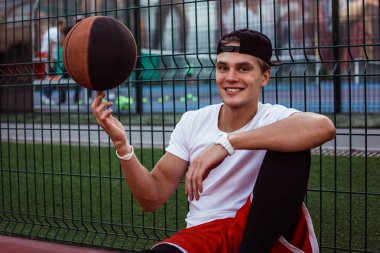 Etrafında dönüyor. Yakışıklı delikanlı turuncu topu tutarak ve basketbol sahası üzerinde dinlenme süre gülümseme ile kameraya seyir spor giyim 