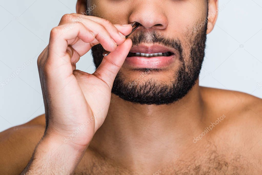Pampering is important for every man. Part of handsome shirtless young black man removing hair from his nose while standing against white background