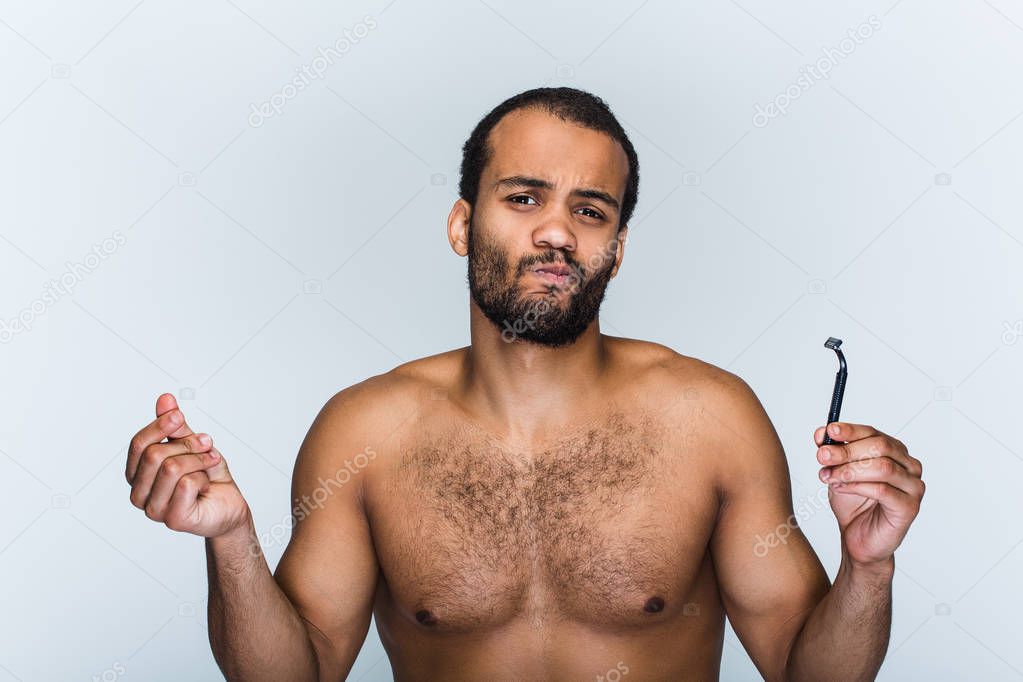 Dont like this razor. Portrait of handsome shirtless young black man looking at camera and holding razor while standing against white background