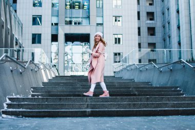 Şehirde yürümek. Güzel genç kadının ayakta açık havada süre gülümseme ile kameraya bakarak pembe ceket tam uzunlukta.