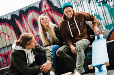 Pazar günü eğleniyor. Bir grup genç insan birbirinizle açık havada kaykay parkta otururken gülümseme ile konuşmak