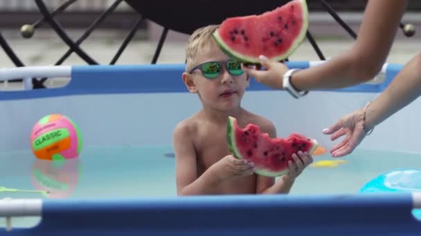 Niño en gafas negras come sandía en la piscina — Vídeo de stock