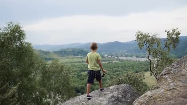 Мальчик стоит на вершине горы и смотрит на бинокль — стоковое видео