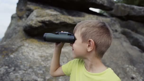 Der Junge steht auf dem Gipfel des Berges und blickt auf das Fernglas — Stockvideo