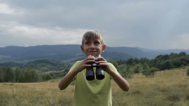 Pojken står på toppen av berget och tittar på kikaren — Stockvideo